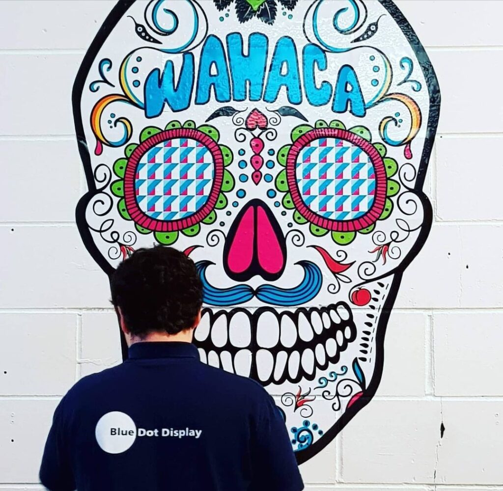 James from Bluedot Display installing a large vinyl wall graphic featuring a skull