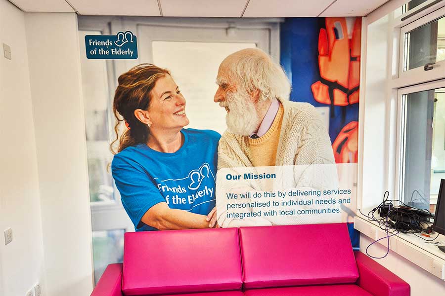 Large vinyl wall wrap showing an elderly visitor to a day care centre in woking speaking to a member of staff